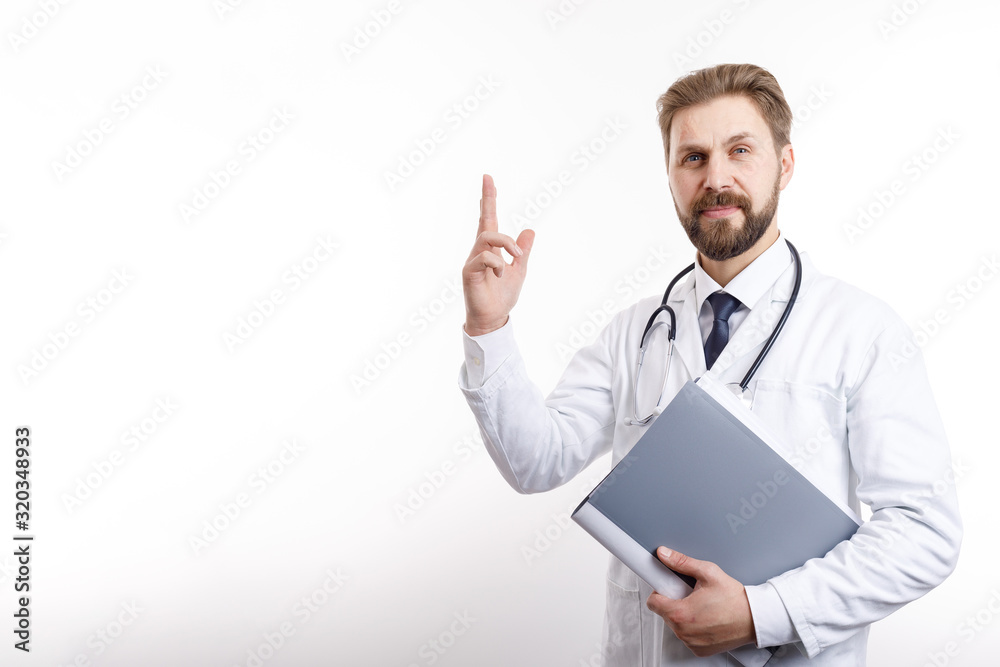 Handsome brown-haired doctor posing with folder and his index finger pointing upwards isolated white background copyspace Handsome brown-haired doctor posing with folder and his index finger pointing upwards isolated white background copyspace