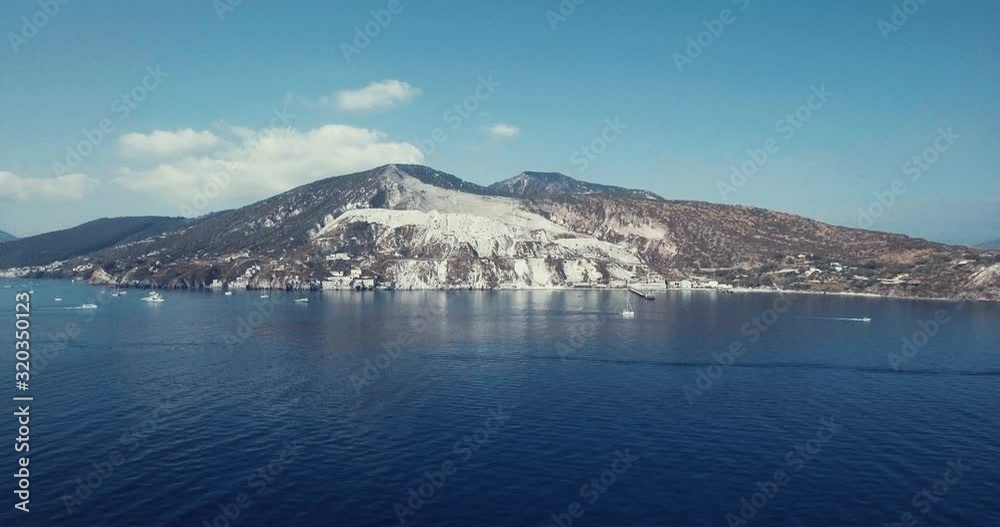 Drone panning view of sailing boats in front the Kaolin quarry in the Mediterranean sea in Lipari, Aeolian islands, Sicily, Italy. Drone is showing a stunning white cliff, beaches and houses. Drone panning view of sailing boats in front the Kaolin quarry in the Mediterranean sea in Lipari, Aeolian islands, Sicily, Italy. Drone is showing a stunning white cliff, beaches and houses.