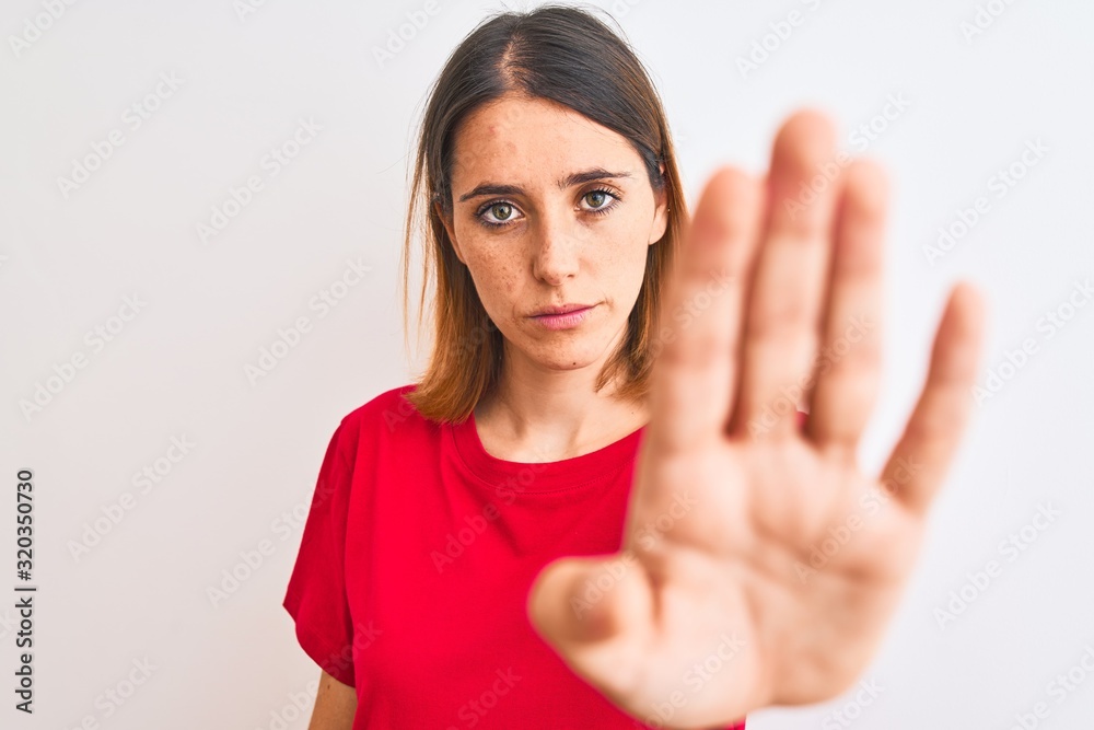 Beautiful redhead woman wearing casual red t-shirt over isolated background doing stop sing with palm of the hand. Warning expression with negative and serious gesture on the face.