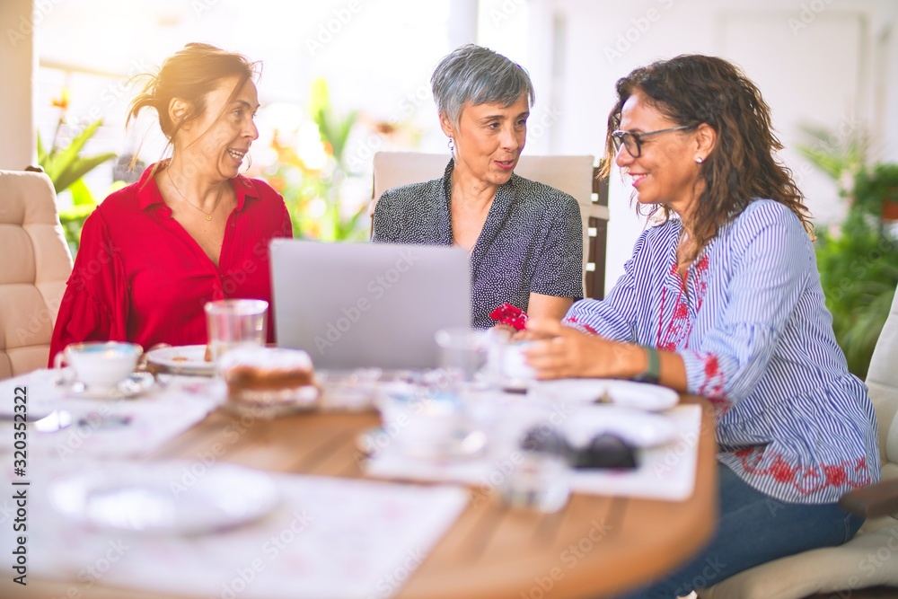 Meeting of middle age women having lunch and drinking coffee. Mature friends smiling happy using laptop at home on a sunny day Meeting of middle age women having lunch and drinking coffee. Mature friends smiling happy using laptop at home on a sunny day