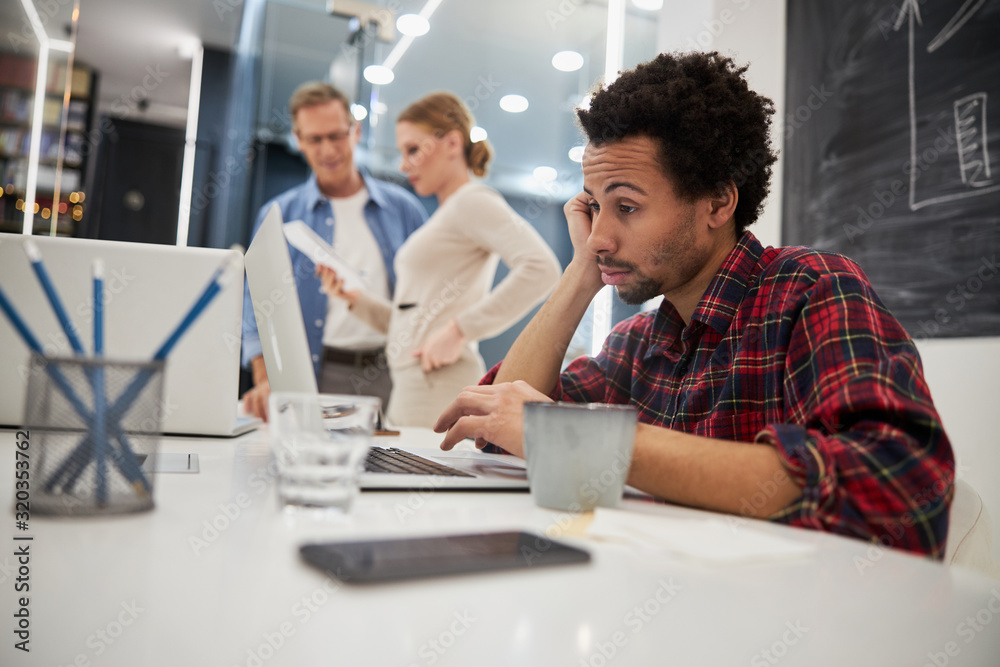 Annoyed afro american man working on notebook in office
