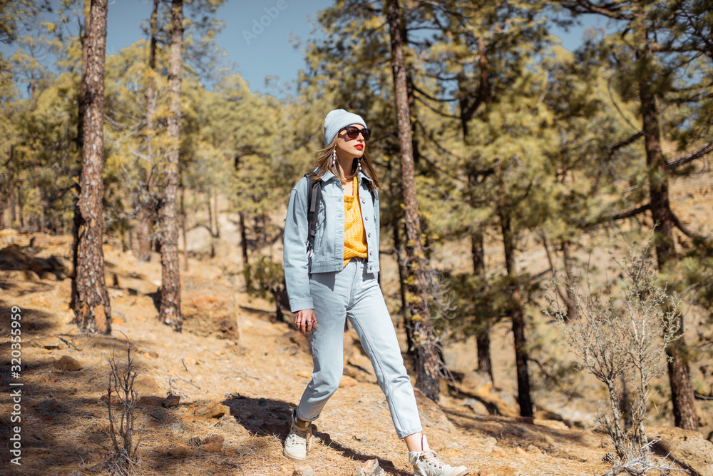 Naklejka premium Young woman dressed casually walking with backpack in the forest highly in the mountains on the volcanic rocks, traveling on Tenerife island, Spain