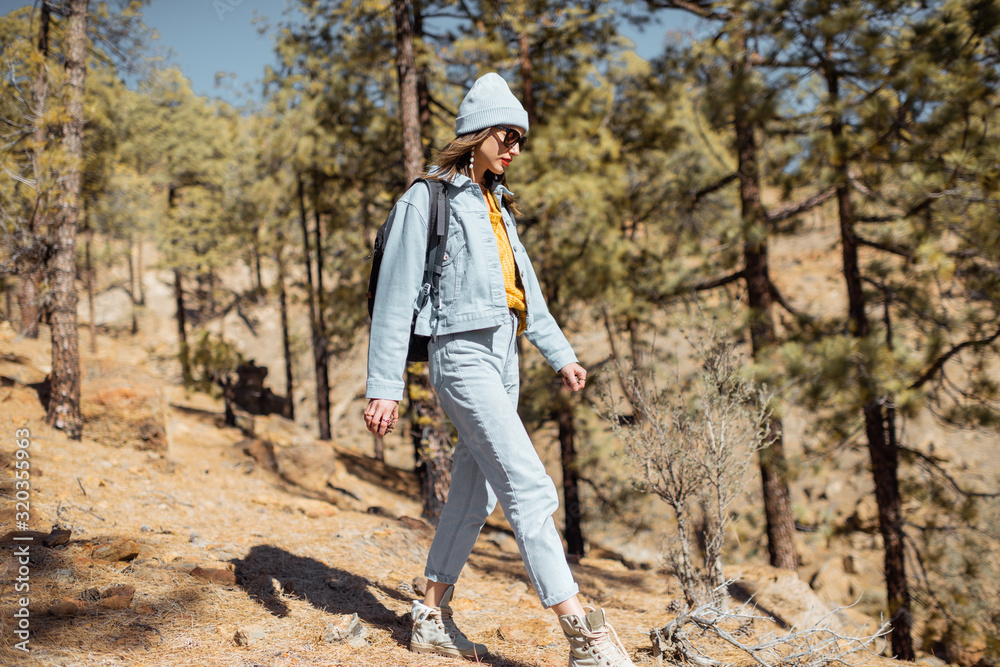 Young woman dressed casually walking with backpack in the forest highly in the mountains on the volcanic rocks, traveling on Tenerife island, Spain