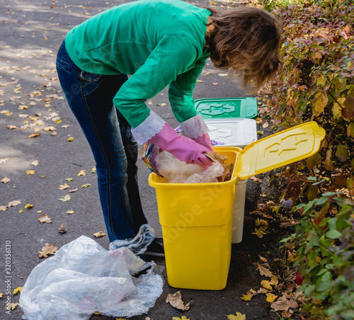 Volunteer girl sorts garbage in the street of the park. Concept of recycling. 