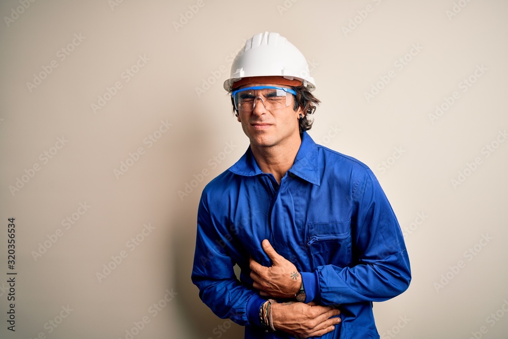 Young constructor man wearing uniform and security helmet over isolated white background with hand on stomach because nausea, painful disease feeling unwell. Ache concept.