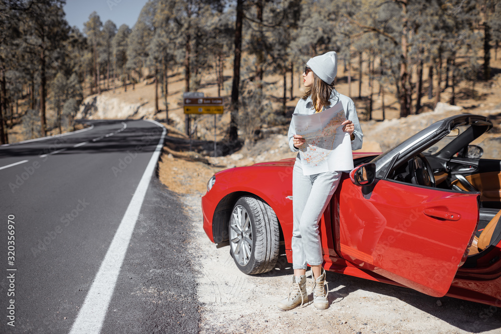 Woman enjoying road trip, standing with map near convertible car on the roadside in the volcanic mountain forest on Tenerife island, Spain Woman enjoying road trip, standing with map near convertible car on the roadside in the volcanic mountain forest on Tenerife island, Spain