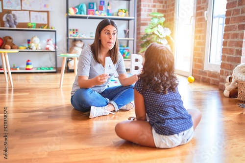 Beautiful teacher teaching alphabet to student toddler girl at kindergarten photo