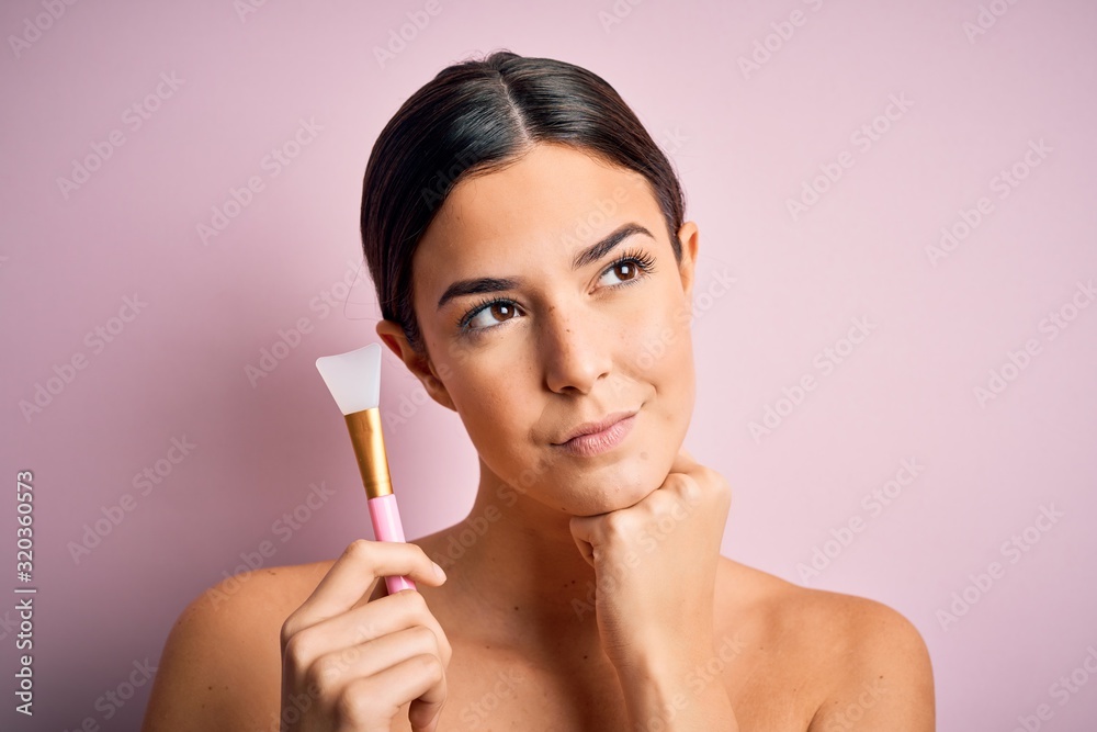 Young beautiful girl applying cosmetic using spatula over pink background serious face thinking about question, very confused idea Young beautiful girl applying cosmetic using spatula over pink background serious face thinking about question, very confused idea