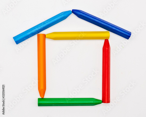 colored wax pencils laid out in the shape of a house on a white background