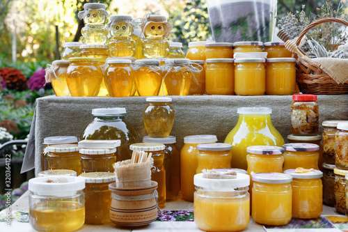 Jars and honey sticks with natural honey on shelf in fair. Sale of natural honey in market outdoor.