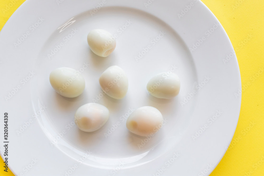 Set of peeled organic small boiled quail eggs on white plate on yellow background. Top view, copy space. Healthy protein fresh natural food. Natural gourmet meal. Little bird eggs. Close up photo. Set of peeled organic small boiled quail eggs on white plate on yellow background. Top view, copy space. Healthy protein fresh natural food. Natural gourmet meal. Little bird eggs. Close up photo.