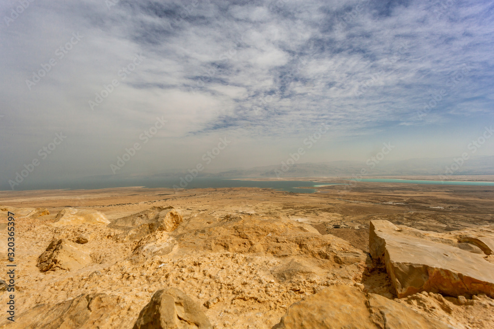 View from the hill to the Dead Sea. The horizon is shrouded in clouds through which you can see the homesteads and mountains. Yellow earth and desert stones