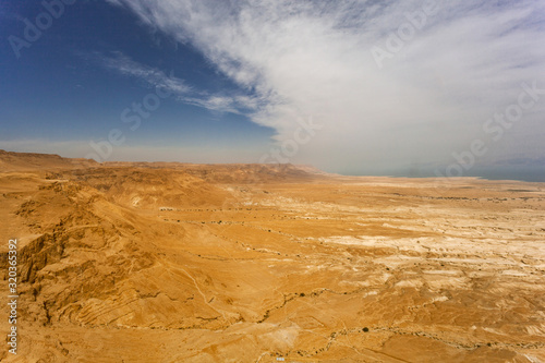 Desert of Israel near the Dead Sea. The dried earth and stones bathed in the sun at its zenith. Over the desert horizon white clouds. Beautiful desert view of travel routes