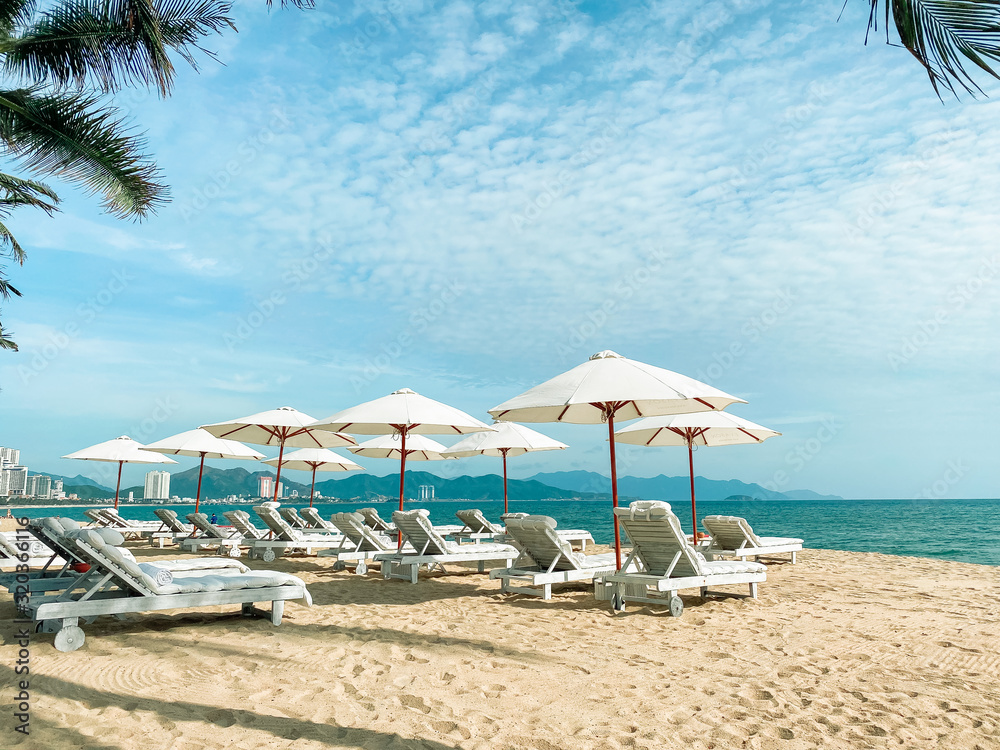 Fototapeta premium White soft sun loungers on the shore of a sandy sea beach. Tropical resort