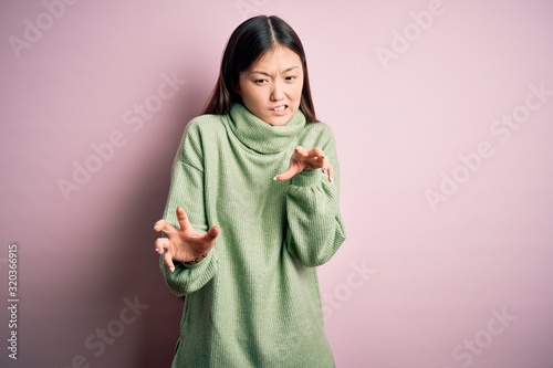 Young beautiful asian woman wearing green winter sweater over pink solated background disgusted expression, displeased and fearful doing disgust face because aversion reaction.
