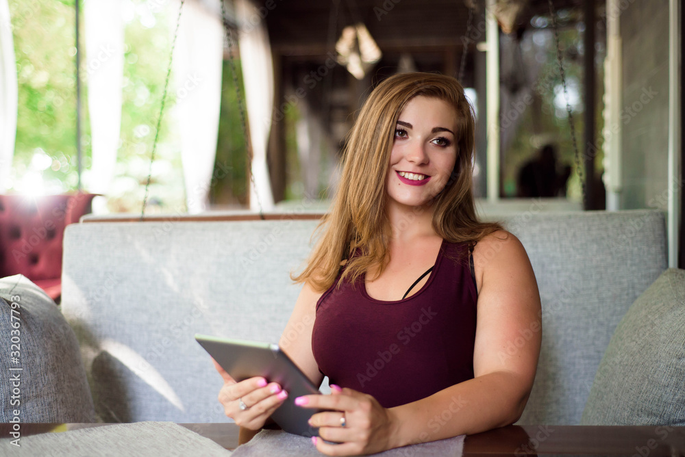 Obraz premium Everyday look. Plus size model. Beautiful young woman with a tablet in a restaurant.