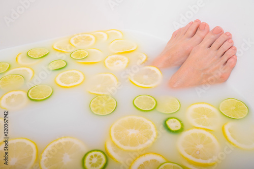 Girl takes a milk bath with lemons and limes. Citrus spa. Body care. Skin whitening. Women's feet.