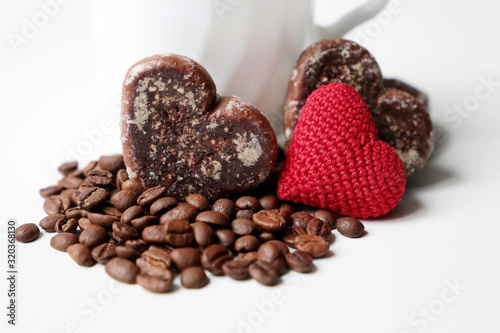 Valentine day romantic breakfast, cup of coffee, red knitted heart and gingerbreads with coffee beans on white background. Concept of love and care, morning dessert