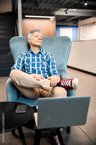 Mature man is sitting in armchair and relaxing