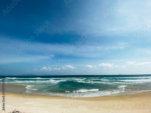 Sandy seashore  calm soft waves at sea  sunny weather  blue sky with white clouds