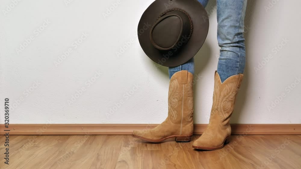 men in western boots stands in front of the wall with a hat in hand and knocks on the floor.