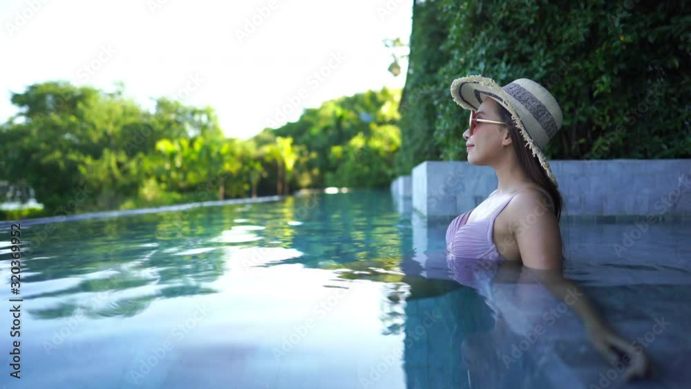 Side view of an Asian woman sitting in a resort infinity pool with hat Side view of an Asian woman sitting in a resort infinity pool with hat