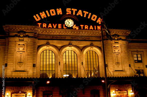 Union Station in Denver, Colorado at night as the sign is illuminated in orange and pierces the dark sky. 