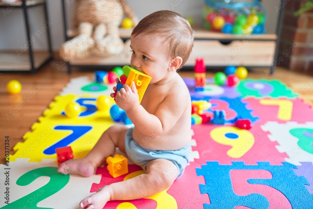 Fototapeta premium Beautiful toddler sitting on puzzle carpet playing with building blocks at kindergarten