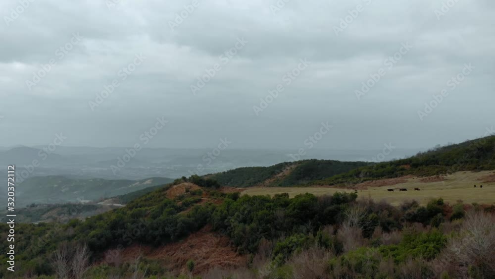 Peaceful rural landscape with green hills around brown pastures with dried grass under rainy clouds, aerial view Peaceful rural landscape with green hills around brown pastures with dried grass under rainy clouds, aerial view