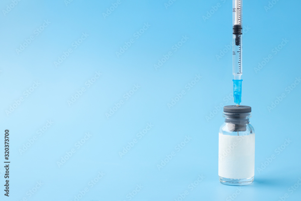 Medical glass bottle with copy space, with syringe inserted, on a blue background. Selective focus. Medical vial for injection with a syringe. Medical glass bottle with copy space, with syringe inserted, on a blue background. Selective focus. Medical vial for injection with a syringe.
