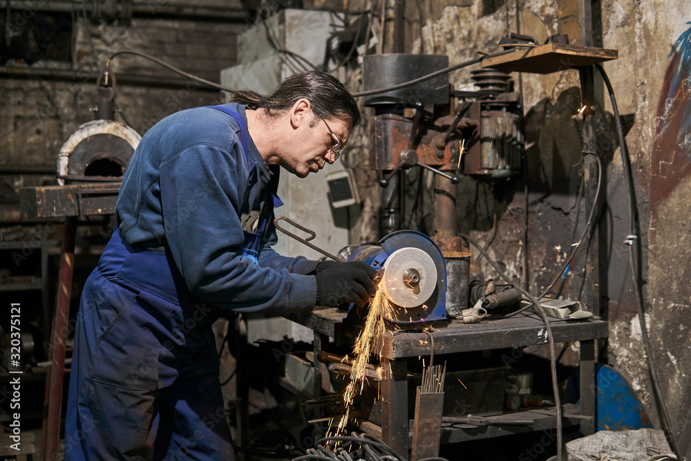 handicraftsman processes a blacksmith's tool on a power grinding wheel handicraftsman processes a blacksmith's tool on a power grinding wheel