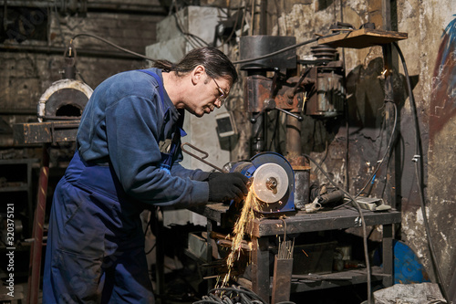 handicraftsman processes a blacksmith's tool on a power grinding wheel