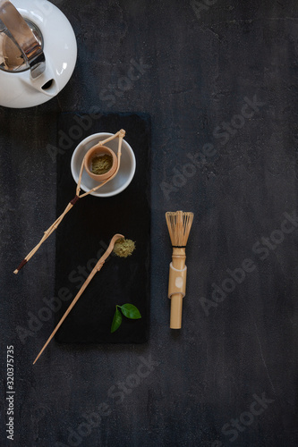 Matcha green tea ceremony set matcha powder, wooden spoon, strainer and whisk on a dark gray background.