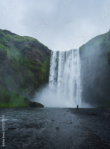 Majestic skogafoss in Iceland, cloudy day with tourist in front