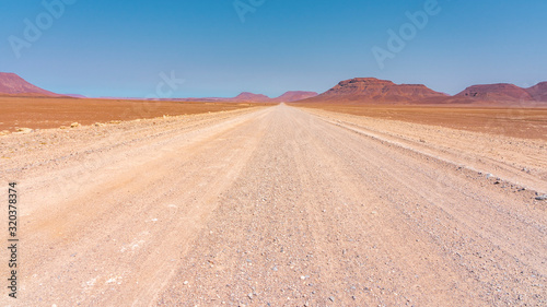 Gravel road in Damaraland in Namibia with red rock mountains. From Palmwag to Sprinbokwasser.