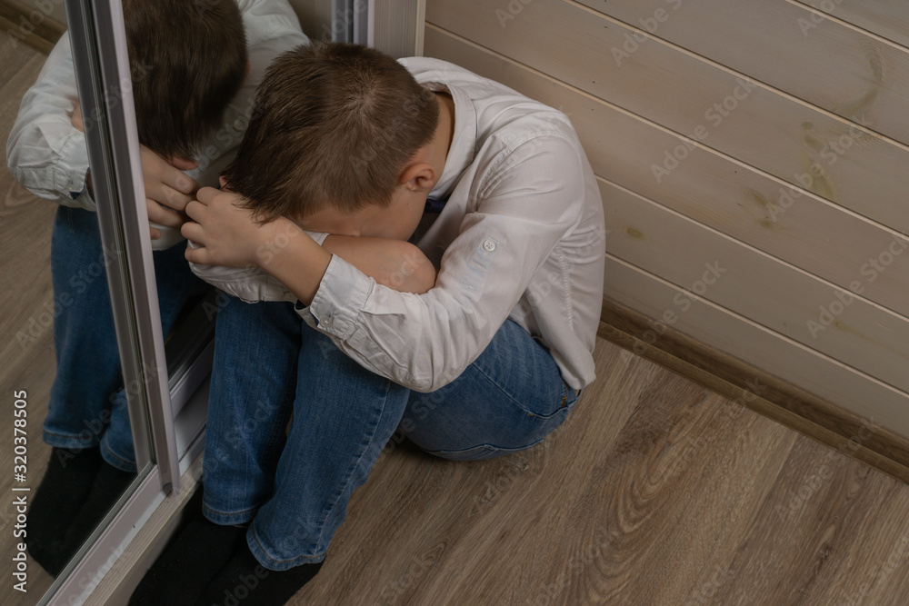 A boy of 10 years old is sitting on the floor upset as a result of bullying. A boy of 10 years old is sitting on the floor upset as a result of bullying.