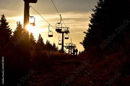 People walks under ski chair lift in the mountains at sunset.
