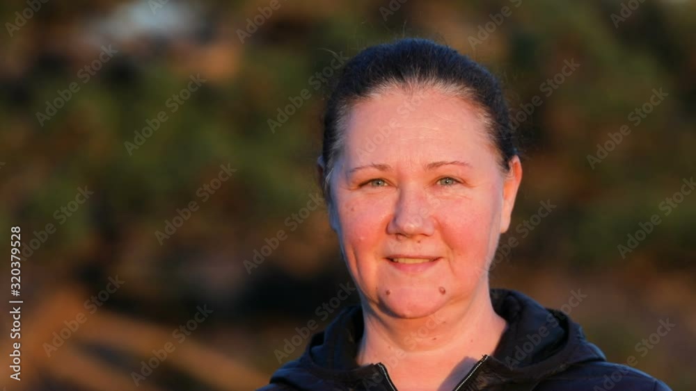 middle-aged woman with tied hair enters the frame and smiles in to the camera and get out , outside in the park on a sunny day middle-aged woman with tied hair enters the frame and smiles in to the camera and get out , outside in the park on a sunny day