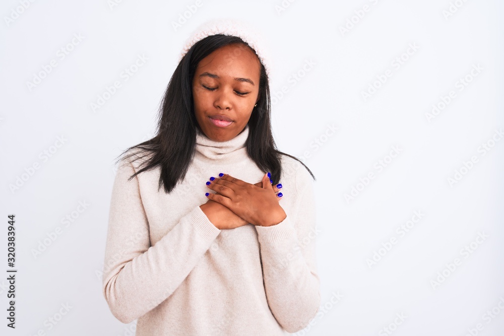 Beautiful young african american woman wearing turtleneck sweater and winter hat smiling with hands on chest with closed eyes and grateful gesture on face. Health concept. Beautiful young african american woman wearing turtleneck sweater and winter hat smiling with hands on chest with closed eyes and grateful gesture on face. Health concept.