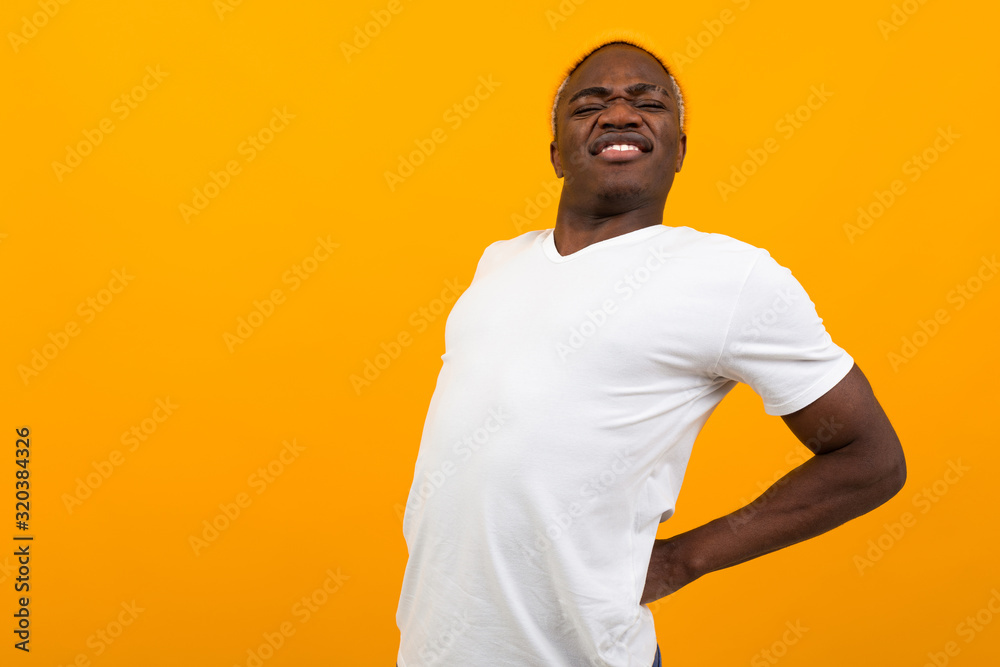 handsome charming black american man in white t-shirt sips his back on yellow isolated background with copy space handsome charming black american man in white t-shirt sips his back on yellow isolated background with copy space