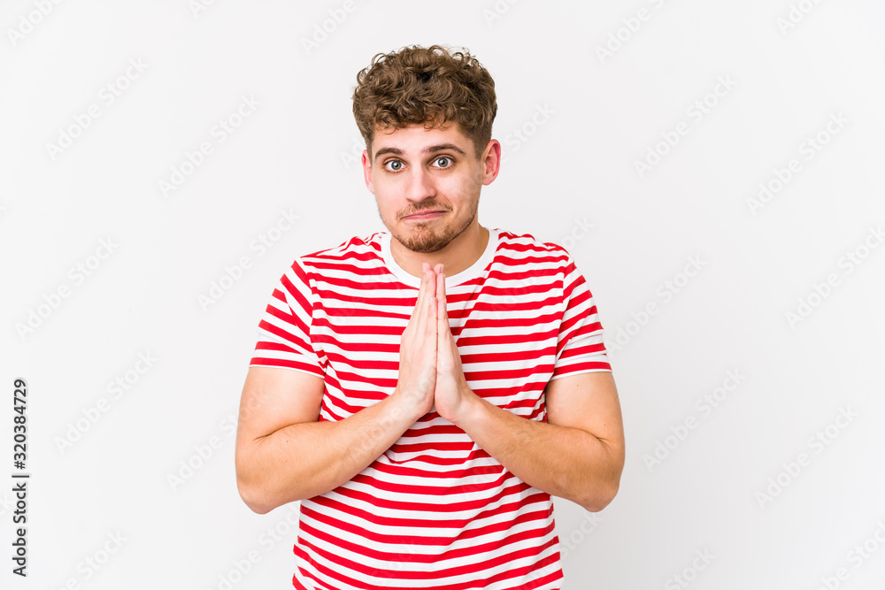 Young blond curly hair caucasian man isolated praying, showing devotion, religious person looking for divine inspiration. Young blond curly hair caucasian man isolated praying, showing devotion, religious person looking for divine inspiration.