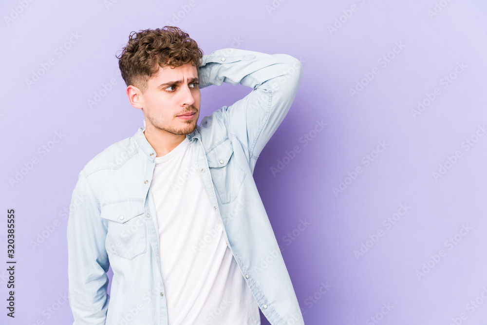 Young blond curly hair caucasian man isolated touching back of head, thinking and making a choice.