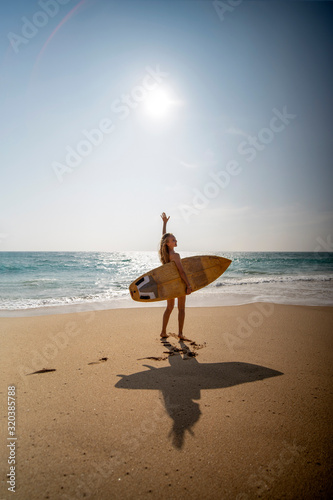 Canvas Print A young woman walks along the beach with a surfboard on the background of the oc