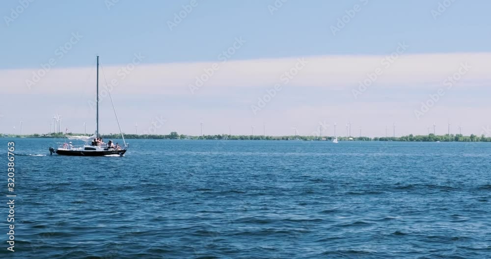 Slow motion shot of a small yacht floating through a bay with wind turbines spinning in the background Slow motion shot of a small yacht floating through a bay with wind turbines spinning in the background