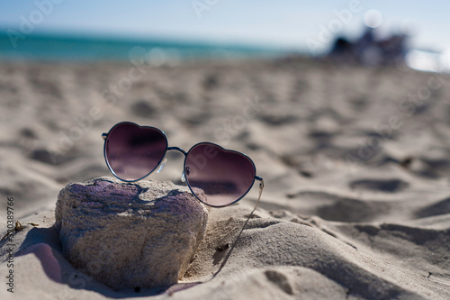 Heart Shape Cool Sunglasses in the sand on a tropical white sand beach. Vacation sunglasses.