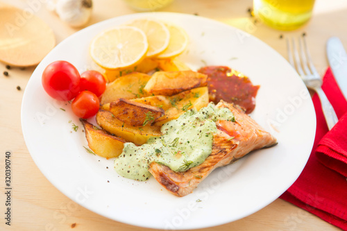 Salmon filet with baked potatoes on plate on wooden table
