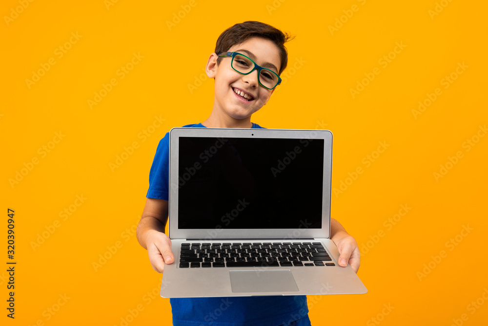 smiling caucasian boy shows laptop screen with mockup on yellow studio background with copy space smiling caucasian boy shows laptop screen with mockup on yellow studio background with copy space