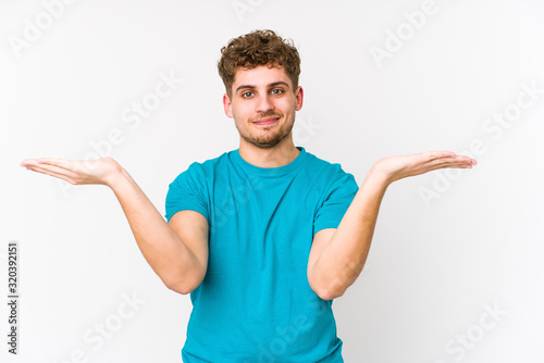 Young blond curly hair caucasian man isolated makes scale with arms, feels happy and confident.