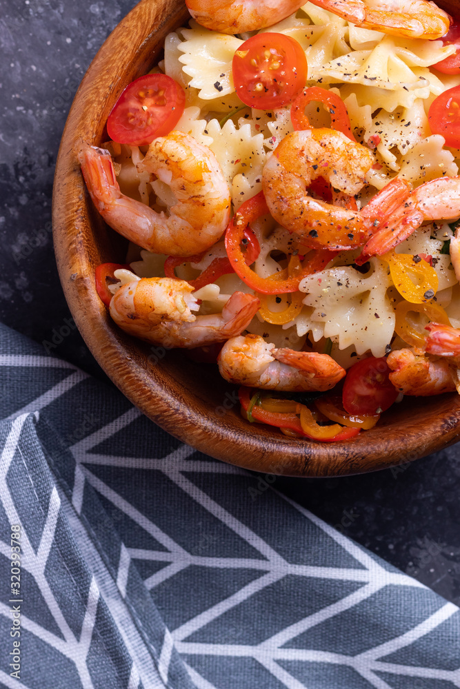 Farfalle pasta with shrimp and spinach and cherry tomatoes in a wooden plate Farfalle pasta with shrimp and spinach and cherry tomatoes in a wooden plate