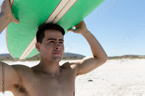 Young man carrying a surfboard at the beach #320395300